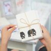 Hands holding the Elephant Dung Letter Writing Set, tied with twine and featuring black elephant silhouettes on the front card.