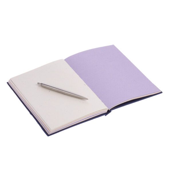 A Large Colourful Elephant Dung Notebook lies open on a white surface, with a silver pen gracefully resting across its blank pages.