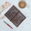 A naturally dyed, handmade Tree of Life Leather Journal by Paper High with flowers and a pen.