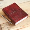 The Large Ganesh Leather Journal, embossed with a Ganesh design, sits elegantly beside a silver pen on the wooden surface.