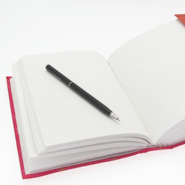 A black pen rests on an open Large Sari Fabric Journal filled with white pages and a striking red cover that exudes elegance.