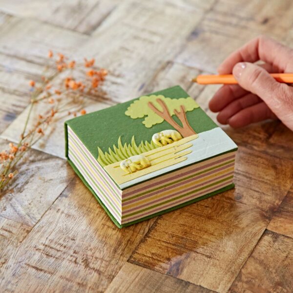 A person writing on a Green Eco Maximus Elephant Dung Notecube with a tree and elephant design by Paper High.