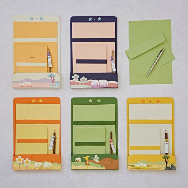 Five Colourful Elephant Dung Letter Writing Sets with matching envelopes, pens, and lined paper sheets arranged on a light surface. Each set features different color schemes and thematic designs, perfect for adding some vibrant flair to your correspondence.