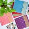 Four Large Sari Fabric Photo Albums in pink, blue, purple, and red are arranged on a white surface with a green plant and scattered photos, creating a vibrant display.