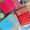 A Medium Sari Fabric Photo Album with button closures is displayed on a wooden surface alongside patterned journals, a succulent, scissors, dried flowers, and printed photos.