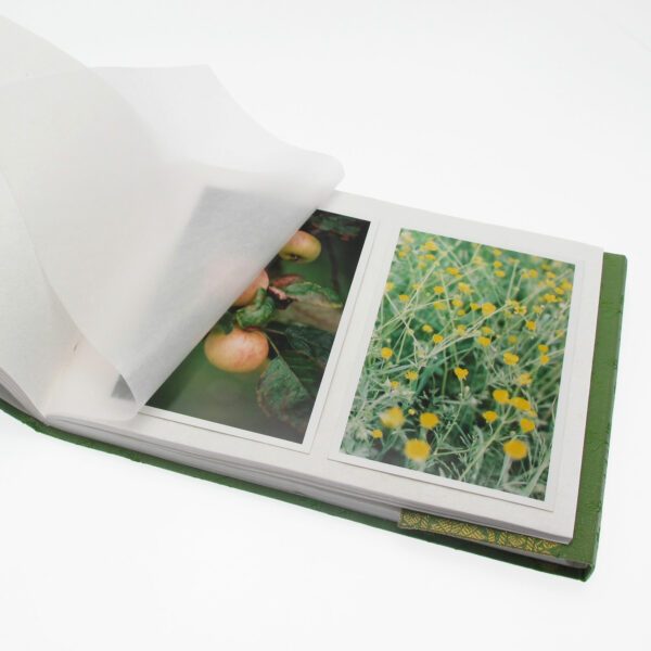 An open Medium Sari Fabric Photo Album displays two photos—apples on a tree and yellow flowers in a field—partially covered by a translucent protective sheet.
