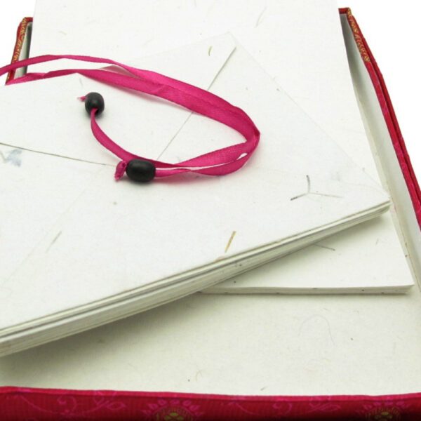 The Sari Letter Writing Set features white envelopes with a pink ribbon and two black beads, elegantly arranged in a red decorative box.