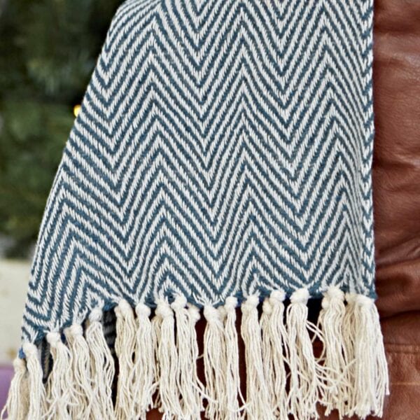 The Chevron Recycled Cotton Throw, made from recycled cotton, showcases a navy and white chevron pattern with fringe draping elegantly over a brown surface.