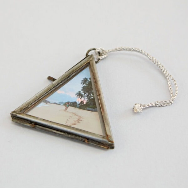An Alia Mini Triangular Glass Hanging Photo Frame, showcasing a beach scene with footprints leading to palm trees and the ocean in the background.