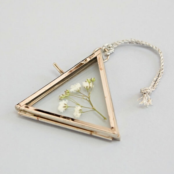 The Alia Mini Triangular Glass Hanging Photo Frame features a silver border encasing delicate white flowers, and is elegantly suspended from a sleek silver cord.