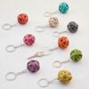 A collection of colorful Recycled Newspaper Ball Keyrings made from woven, recycled material is displayed on a flat surface. A single key is attached to one of the keyrings.