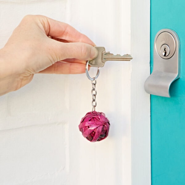 A hand is inserting a key with a Recycled Newspaper Ball Keyring into a turquoise door lock, the keyring crafted from recycled newspapers.