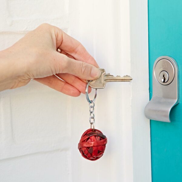 A hand holds a key with a Recycled Newspaper Ball Keyring, inserting it into the lock of a turquoise door.
