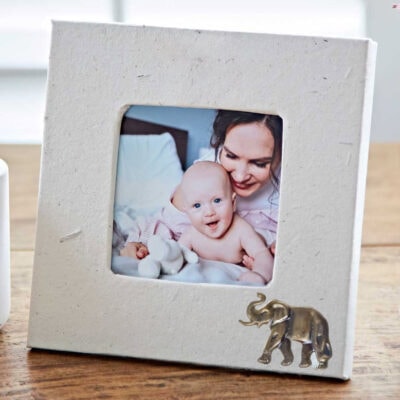 The Elephant Dung Photo Frame displays a smiling baby with an adult, featuring a silver elephant ornament on its border.