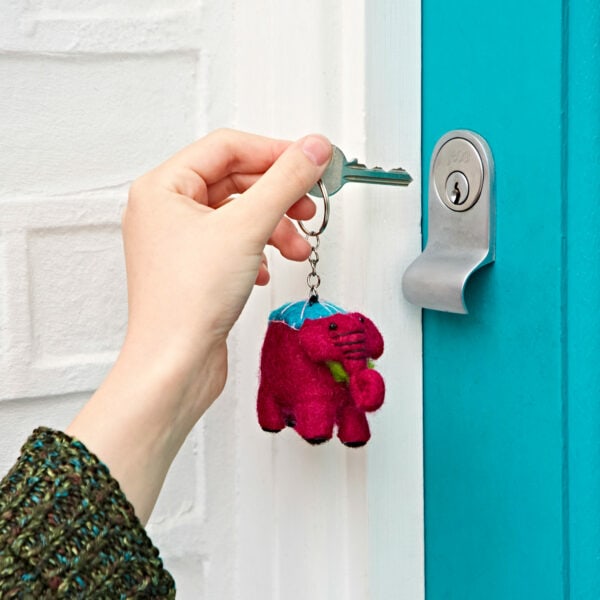 A hand holds a key with a Felt Elephant Keyring beside a turquoise door lock.
