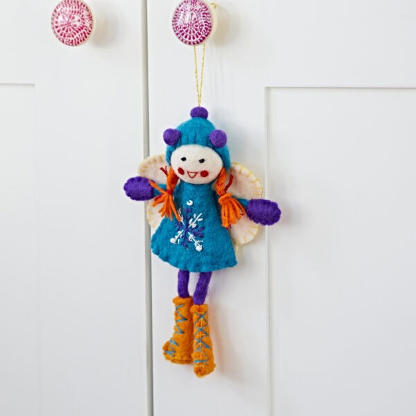 A whimsical Felt Alpine Girl Decoration, featuring a blue dress, purple hat, and orange boots, hangs elegantly on a white cabinet door.
