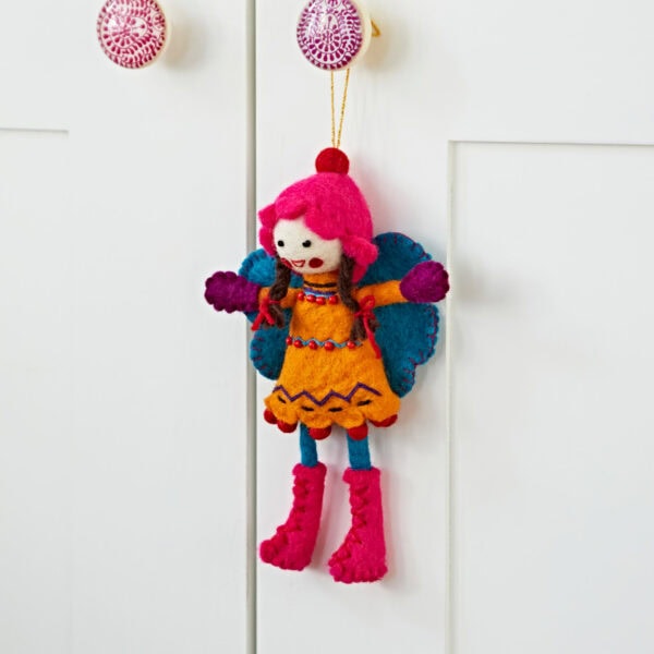 The Felt Alpine Girl Decoration, featuring a vibrant fairy doll with red boots, dangles gracefully on a white cabinet, adding a whimsical touch.