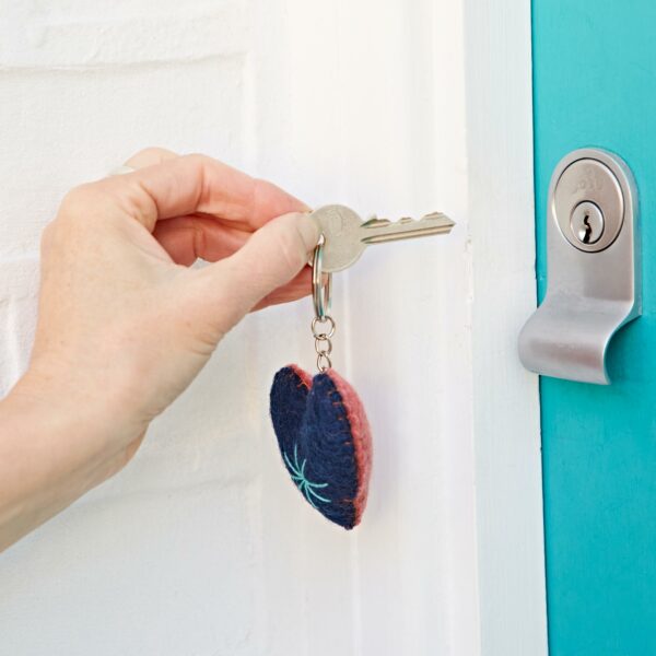 A hand holding a key with a Felt Heart Keyring is inserting the key into a turquoise door lock.