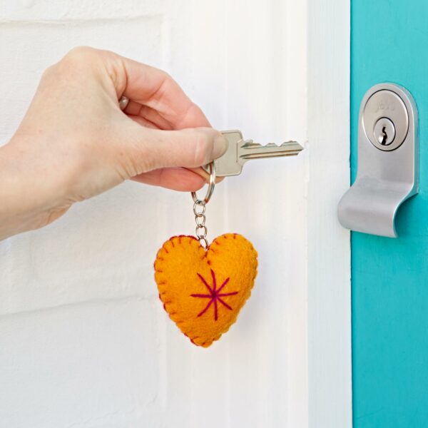 A hand holding a key with a Felt Heart Keyring, about to insert the key into a turquoise door lock.