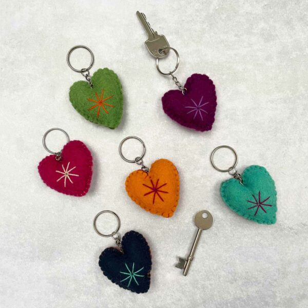 Six colorful Felt Heart Keyrings with star patterns are laid out on a white surface, alongside two silver keys attached to some of the keyrings.