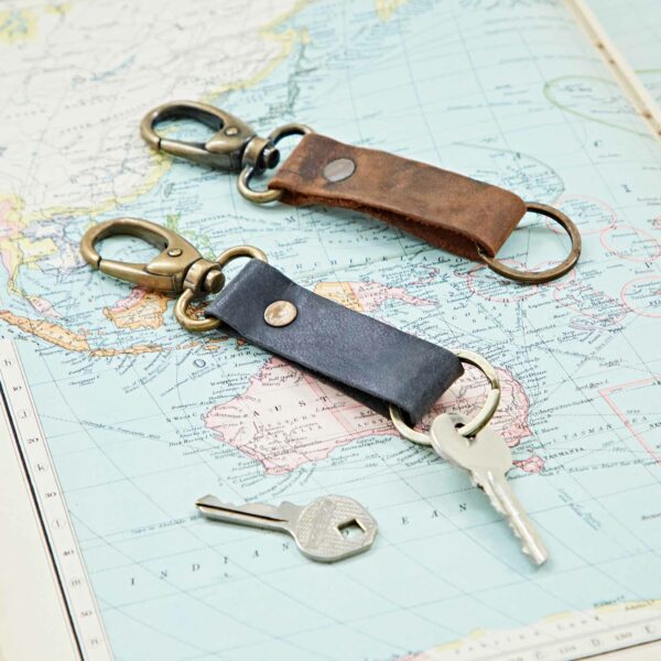 Two leather keychains and a silver key rest on a map of Africa, Europe, and Asia—the ideal backdrop to highlight the Personalised Buffalo Leather Keyring with Hook.