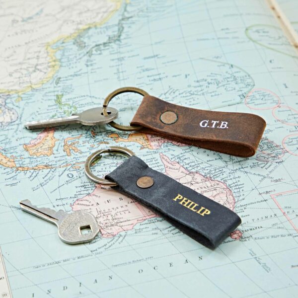 Two Personalised Buffalo Leather Keyrings, labeled "G.T.B." and "PHILIP," rest on a world map featuring regions of Australia and Southeast Asia.