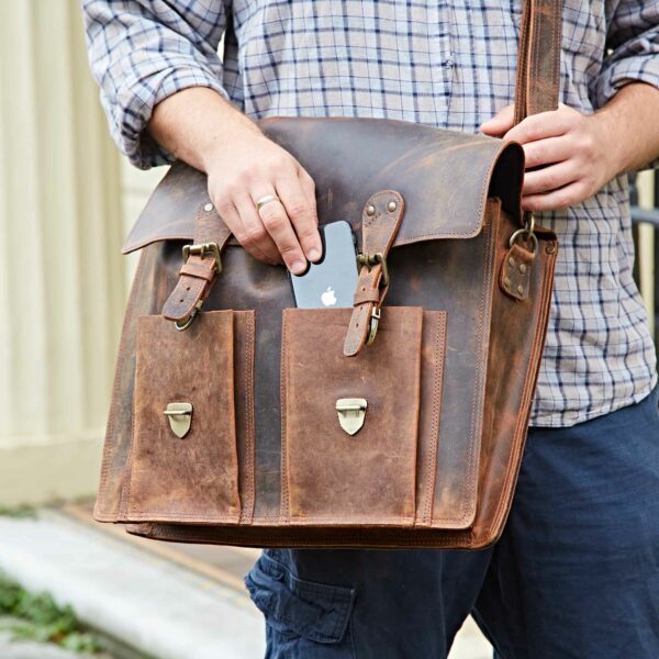 Someone placing an iPhone into the front pocket of a Personalised Brown Buffalo Leather Satchel Style Briefcase outdoors, highlighting the versatility and classic appeal of this handcrafted bag.