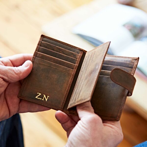 A person holds an open brown buffalo leather credit card wallet with several card slots and the initials "Z.N." embossed in gold on the lower left corner.