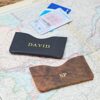 Two Personalised Buffalo Leather Slim Card Holders—one black with "DAVID" and one brown with "SP"—are displayed on a map alongside ID and credit cards.