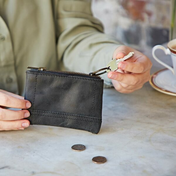 A woman is holding a Buffalo Leather Zipped Purse with Keyring on a table.