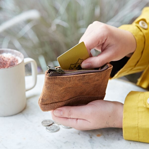A person holding a Personalised Buffalo Leather Zipped Purse and a cup of coffee.