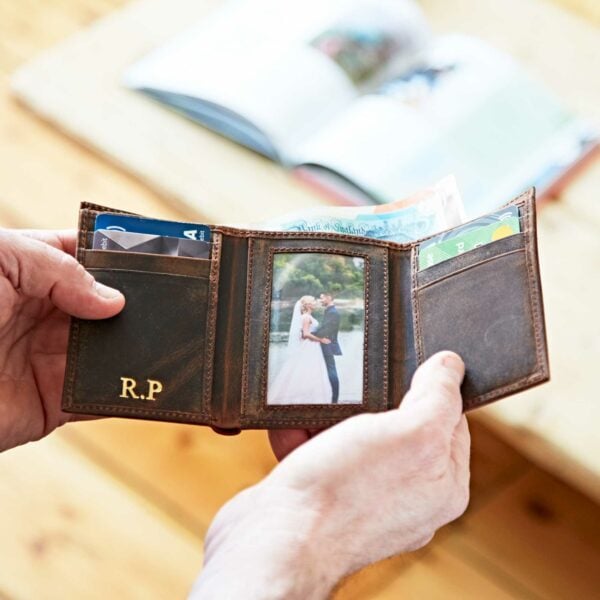 A person holds an open Buffalo Leather Wallet containing cards, cash, and a photo of a couple; the initials "R.P." are embossed on this elegant trifold wallet.