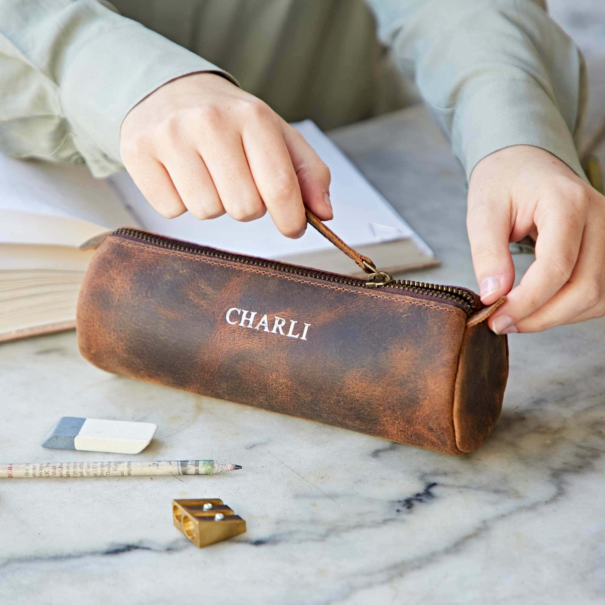 A person is holding a Personalised Buffalo Leather Round Pencil Case on a table.