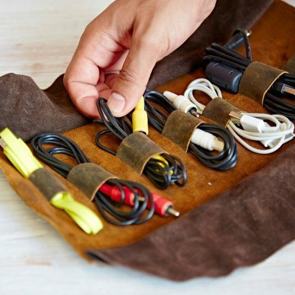 A hand organizing cables and cords secured with straps inside a brown Personalised Buffalo Leather Cable Organiser.