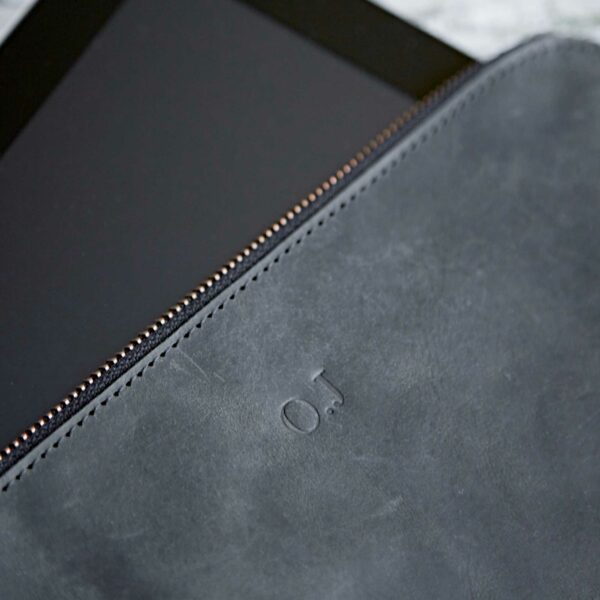 A close-up of the Personalised Buffalo Leather Tablet Case in black, with a zipper, partially covering a tablet. The pouch has subtle embossed "OJ" initials for a personalised touch.