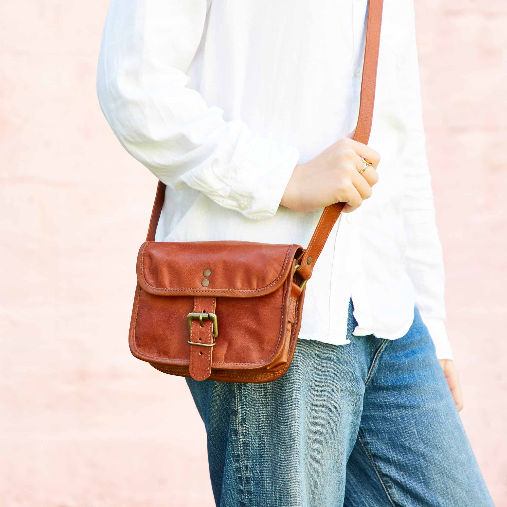 A fashionable person in a white shirt and jeans is carrying the Personalised Brown Leather Crossbody Bag.