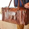 A man is holding a naturally dyed, handmade Personalised Large Leather Holdall with Zipped Pockets