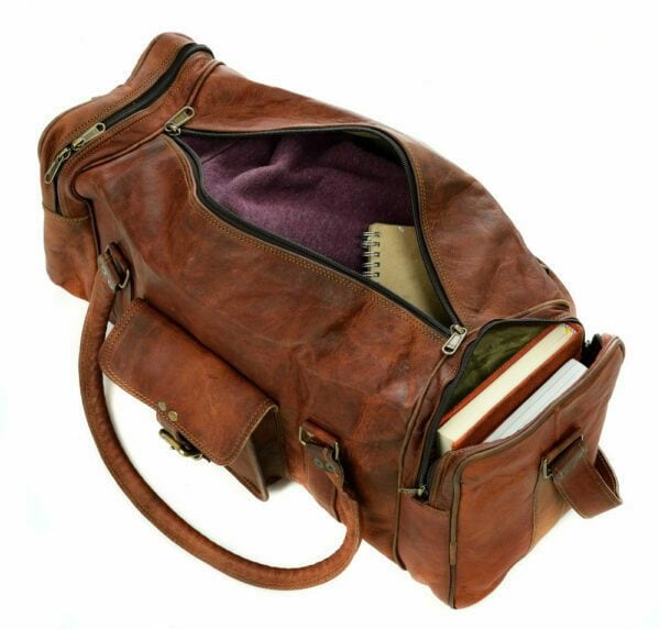 A Personalised Brown Leather Holdall with zipped pockets, featuring a visible notebook, books in an outer pocket, and a purple fabric lining, is photographed on a white background.
