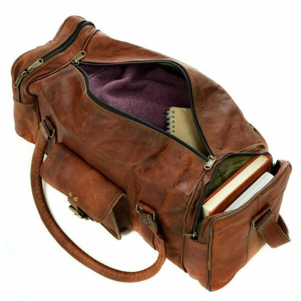 A Personalised Brown Leather Holdall with zipped pockets, featuring a visible notebook, books in an outer pocket, and a purple fabric lining, is photographed on a white background.
