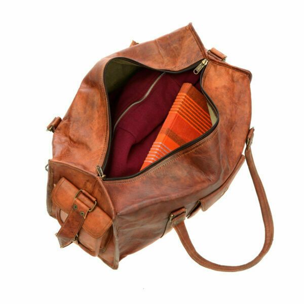 A Personalised Brown Leather Holdall with a shoulder strap sits unzipped on a white background, revealing a red garment and orange striped fabric inside.