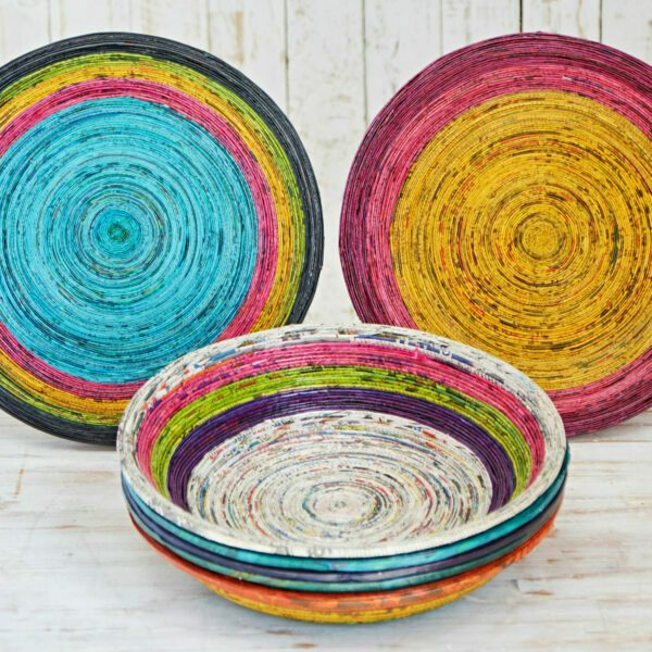 A Round Recycled Newspaper Bowl featuring colorful concentric circular patterns is displayed against a white wooden background, highlighting sustainable craftsmanship.