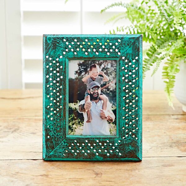 A 6" x 4" Hara Green Distressed Mango Wood Photo Frame is elegantly placed on the wooden table, featuring a heartwarming image of a smiling man with a child on his shoulders.