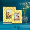 Two Asin Yellow Chevron Patterned Photo Frames with family photos sit on a blue cabinet next to a clear vase filled with small white flowers.