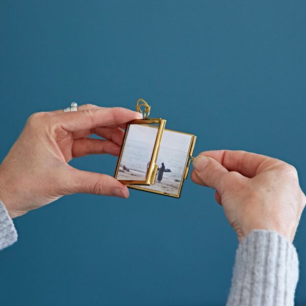 Hands holding an Alia Square Glass Hanging Photo Frames with a photo of a person standing on a beach inside.