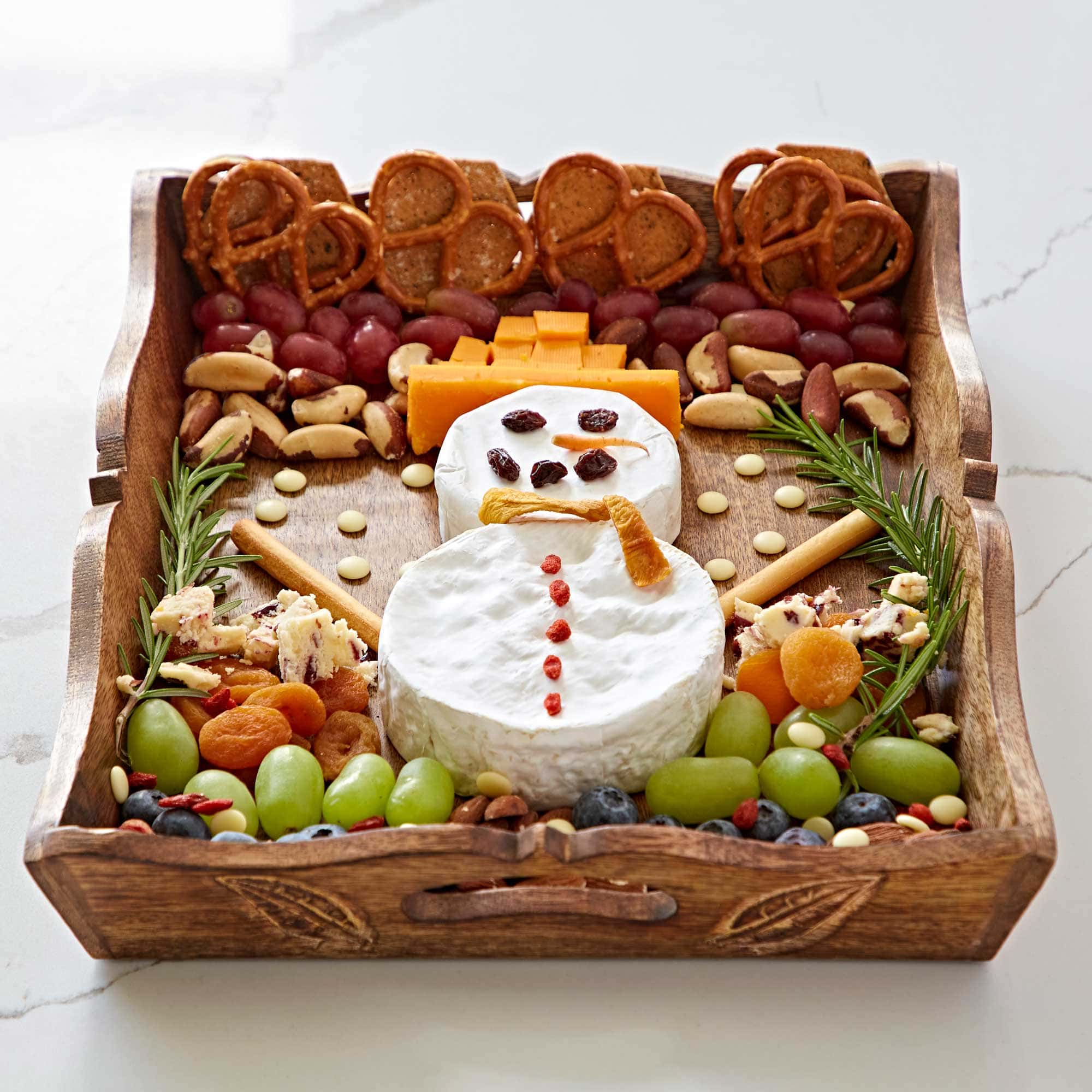 A Natural Mango Wood tea tray with cheese shaped like a snowman, grapes, nuts and pretzels.