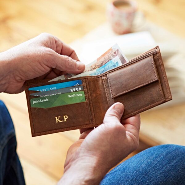 A man is holding a handmade brown, naturally dyed Personalised Leather Wallet by Paper High with money and cards in it.