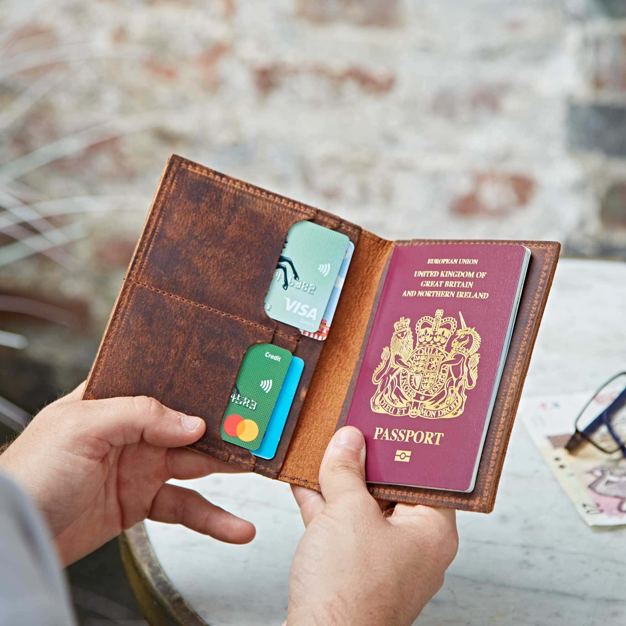 A person holds an open Personalised Buffalo Leather Passport Holder containing a UK passport and three bank cards.