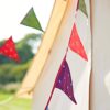 Recycled Sari Bunting, made from vibrant, recycled materials, is elegantly draped diagonally in front of a white tent, with lush greenery and a clear sky forming the perfect backdrop.