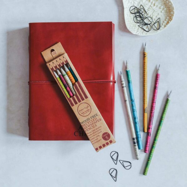 A set of Paper High recycled newspaper pencils on top of a personalised leather journal.