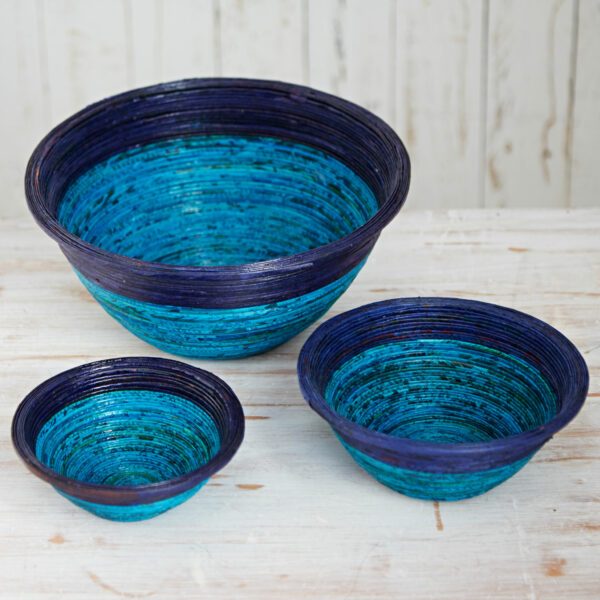 Three nested round bowls in dark blue and light blue stripes are arranged on a rustic white wooden surface with a light wooden background.
